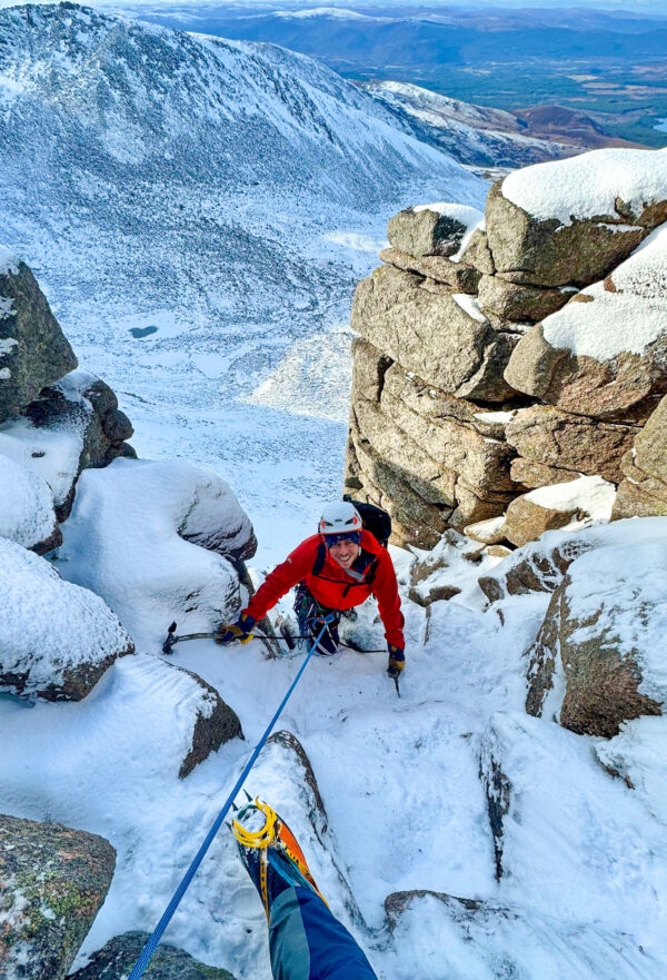 A man smiling as he climbs the crux of a winter route on one of our winter mountain training courses in Aviemore, Scotland.