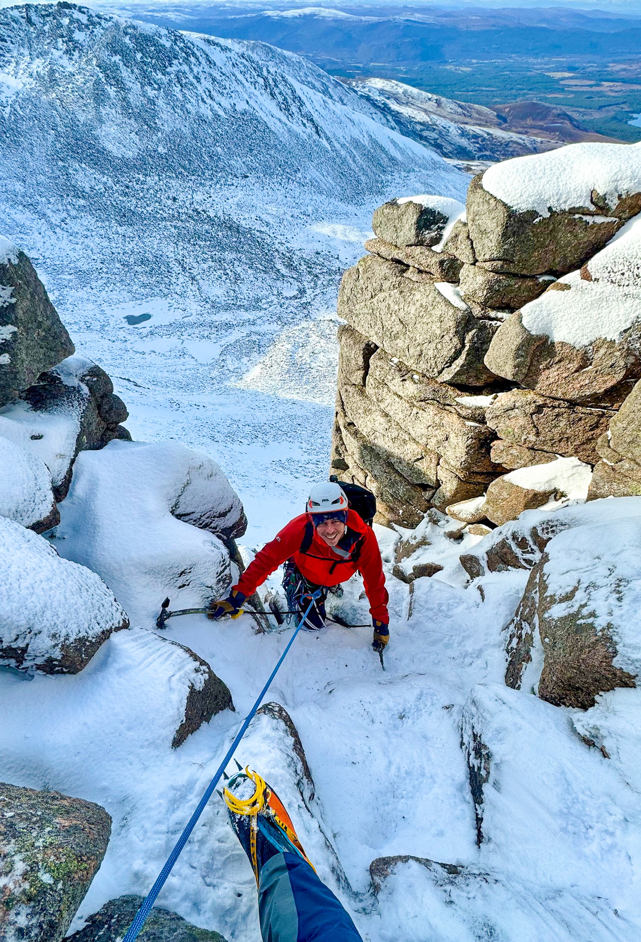 A man smiling as he climbs the crux of a winter route on a winter mountaineering course in Aviemore, Scotland.