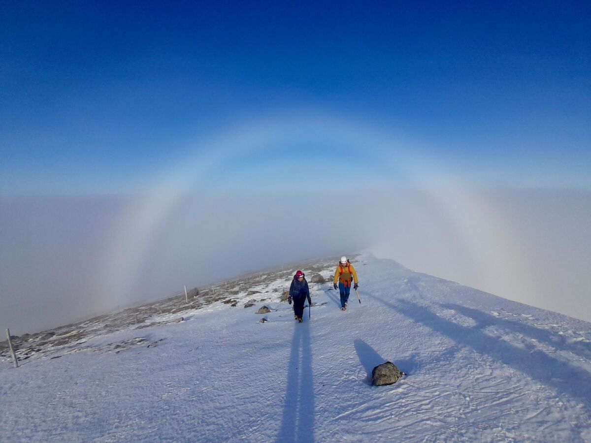 Two walkers with ice axes and crampons with a sun halo on a winter skills course in Scotland.