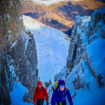 A lady and man climb steep snow on a winter mountaineering course.
