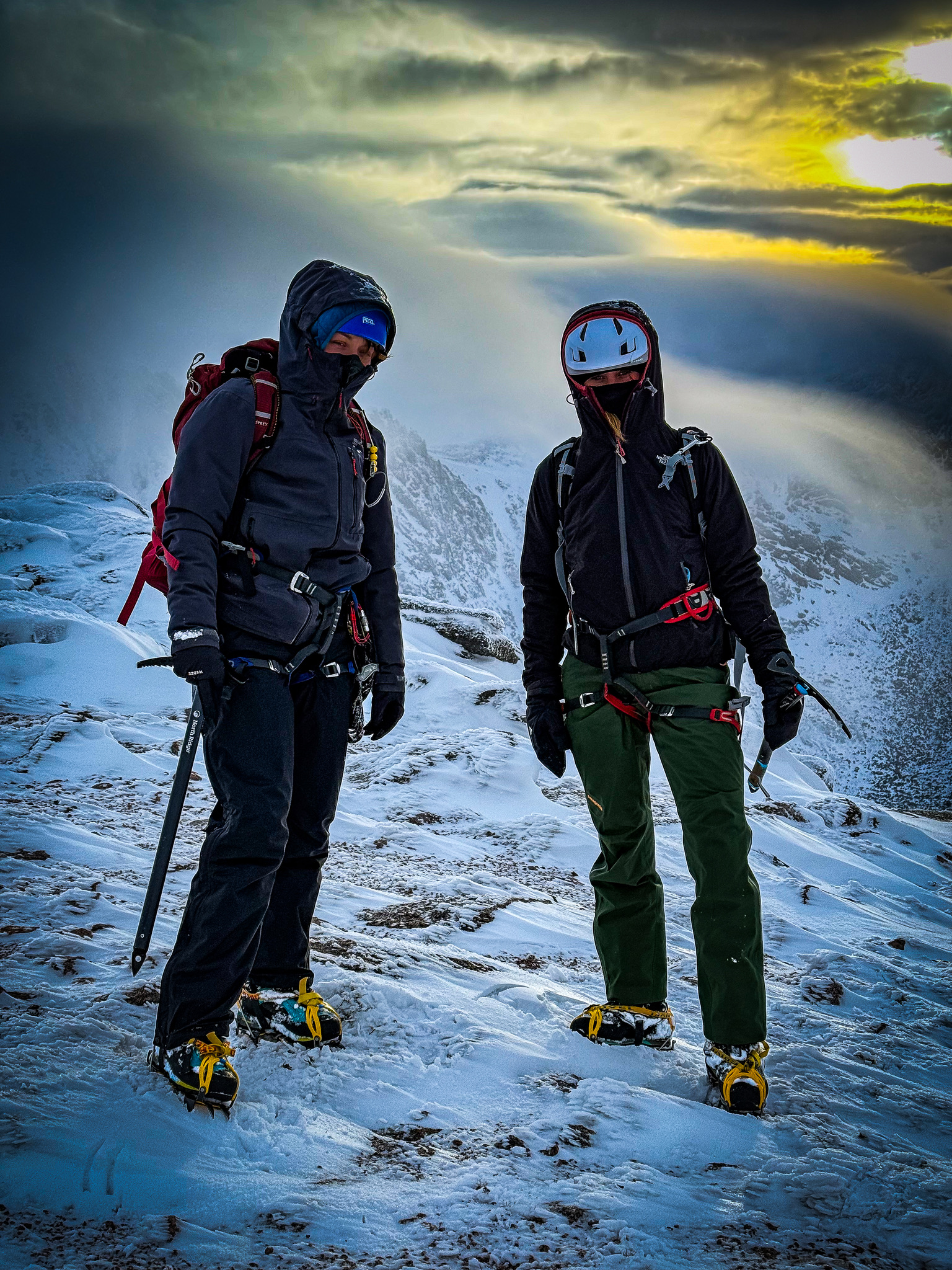 Two ladies stand on Cairngorm in evening light carrying ice axes and wearing crampons whilst on a winter mountaineering course in Scotland.