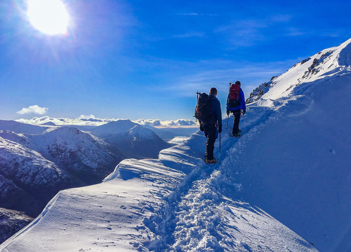 A pair of walkers ascend a snowy ridge with ice axes and crampons on a Winter Skills course in Scotland.