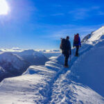 A pair of walkers ascend a snowy ridge with ice axes and crampons on a Winter Skills course in Scotland.