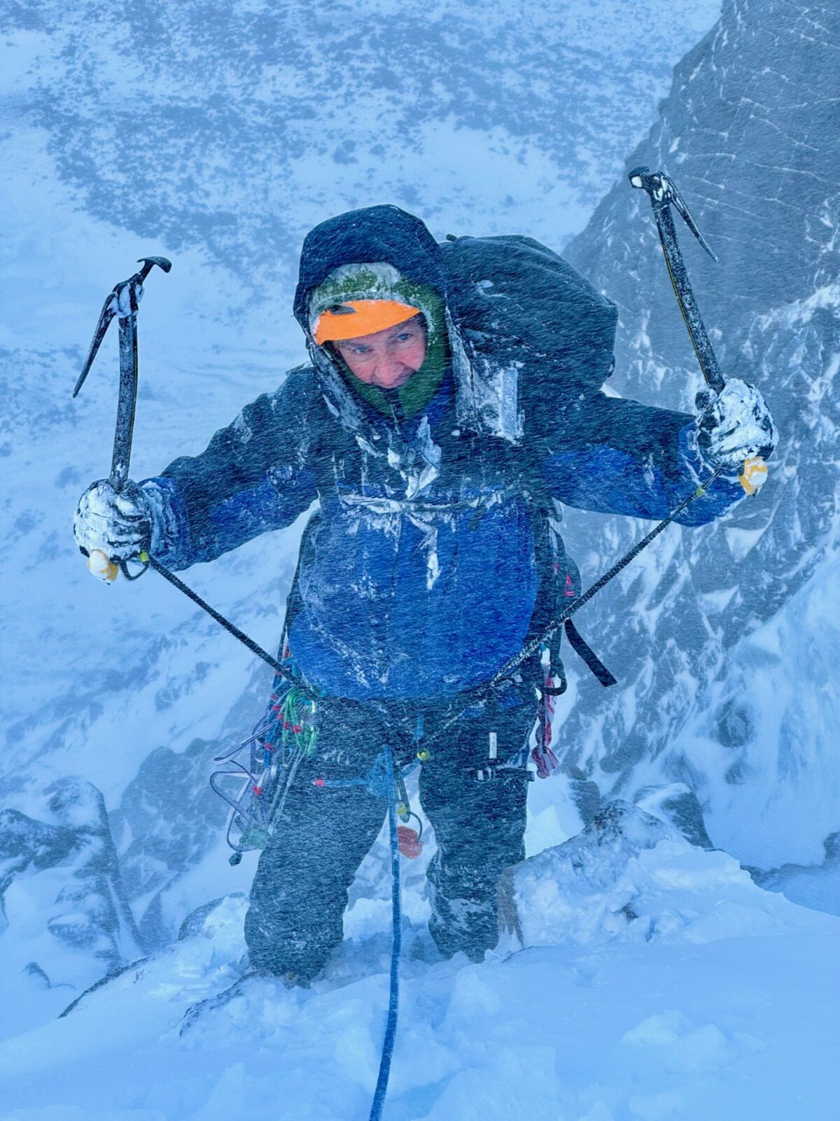 A man brandishing ice axes in a winter storm on a winter mountaineering course in Scotland.