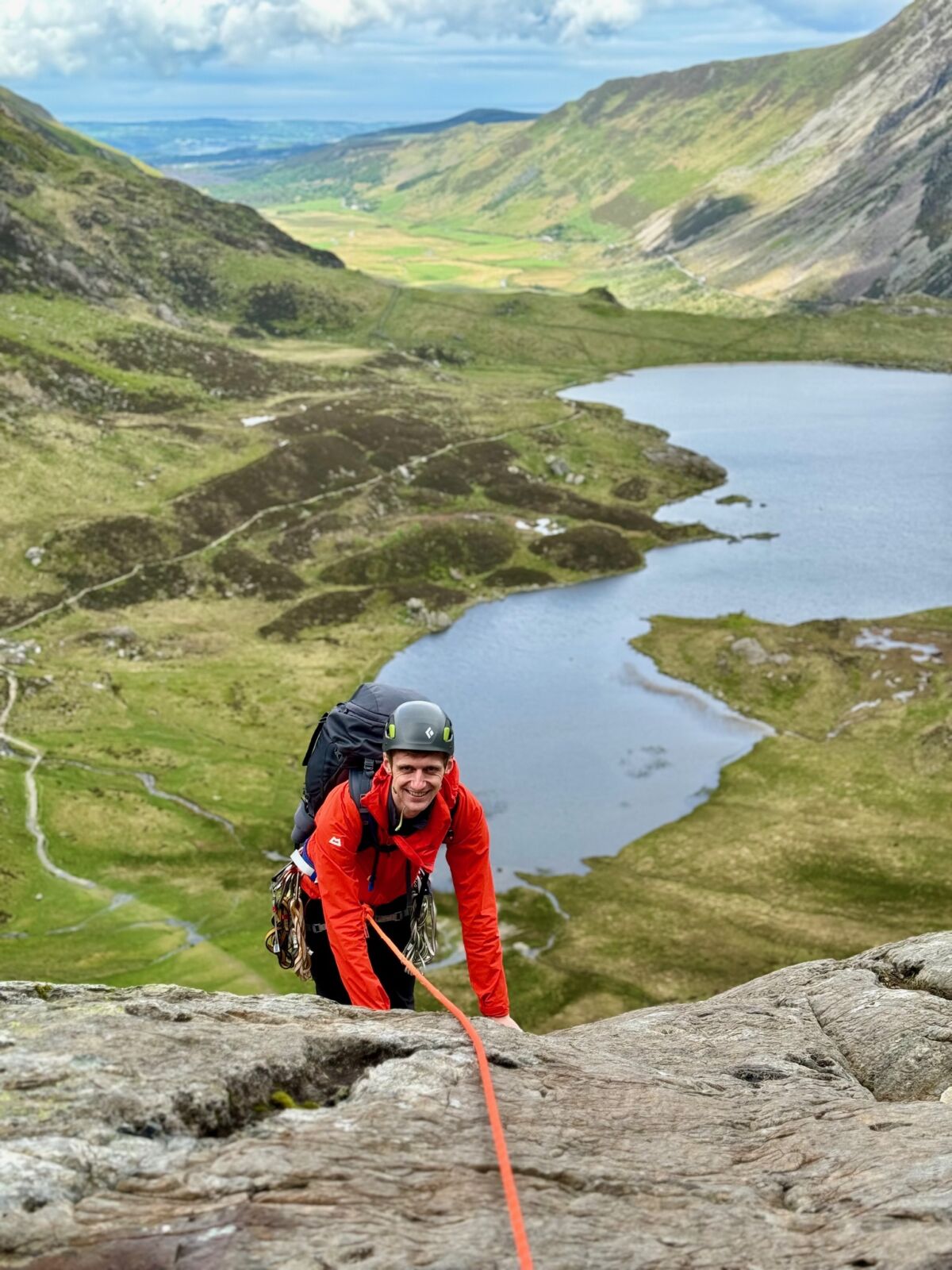 A man scrambles up a rock with a rope on an Advanced Scrambling course in Eryri.