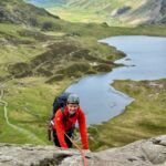 A man scrambles up a rock with a rope on an Advanced Scrambling course in Eryri.
