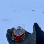 A gloved hand holding a compass in a whiteout in Scotland. #Advanced Navigation.