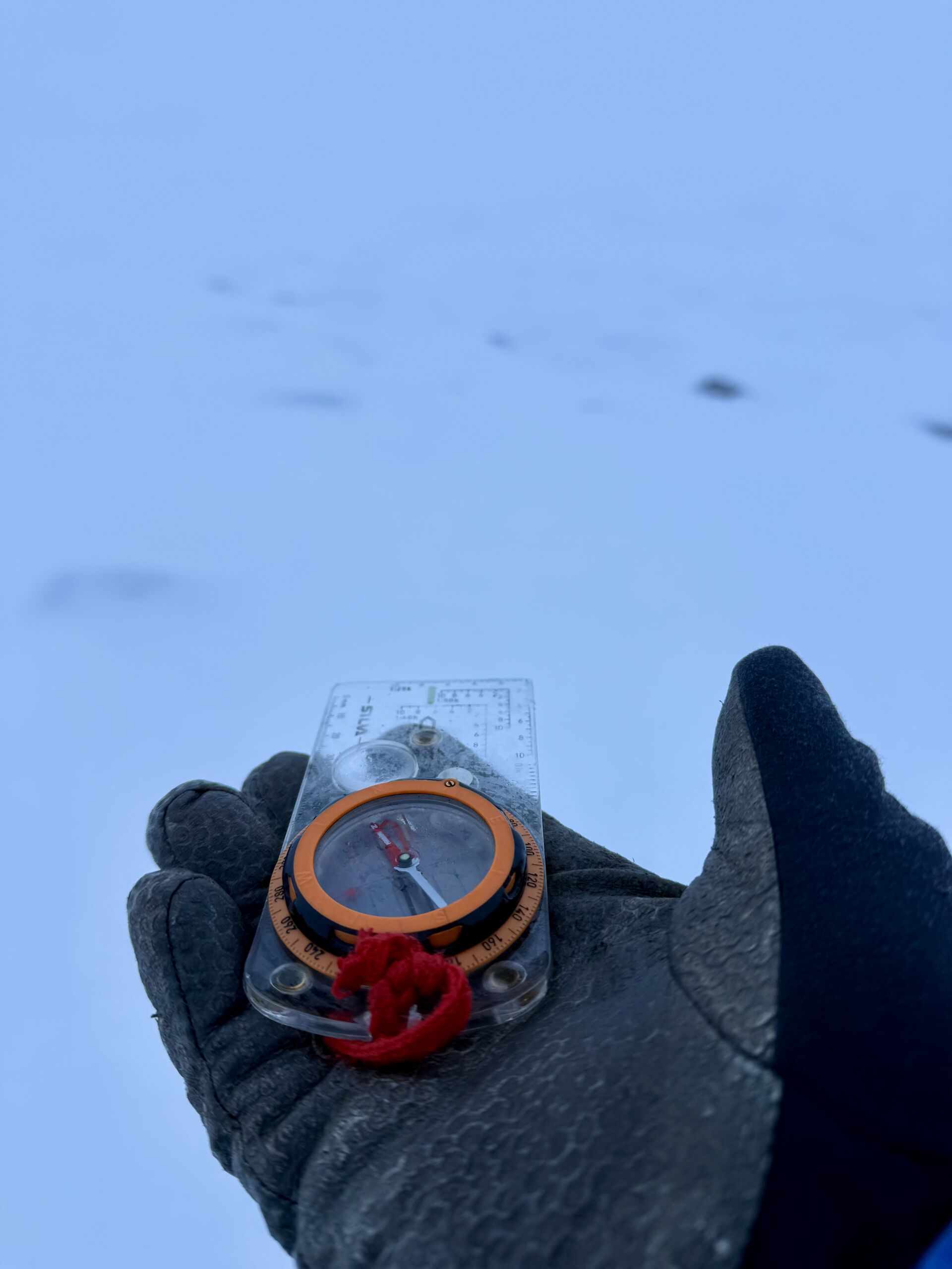 A gloved hand holding a compass in a whiteout in Scotland. #Advanced Navigation.