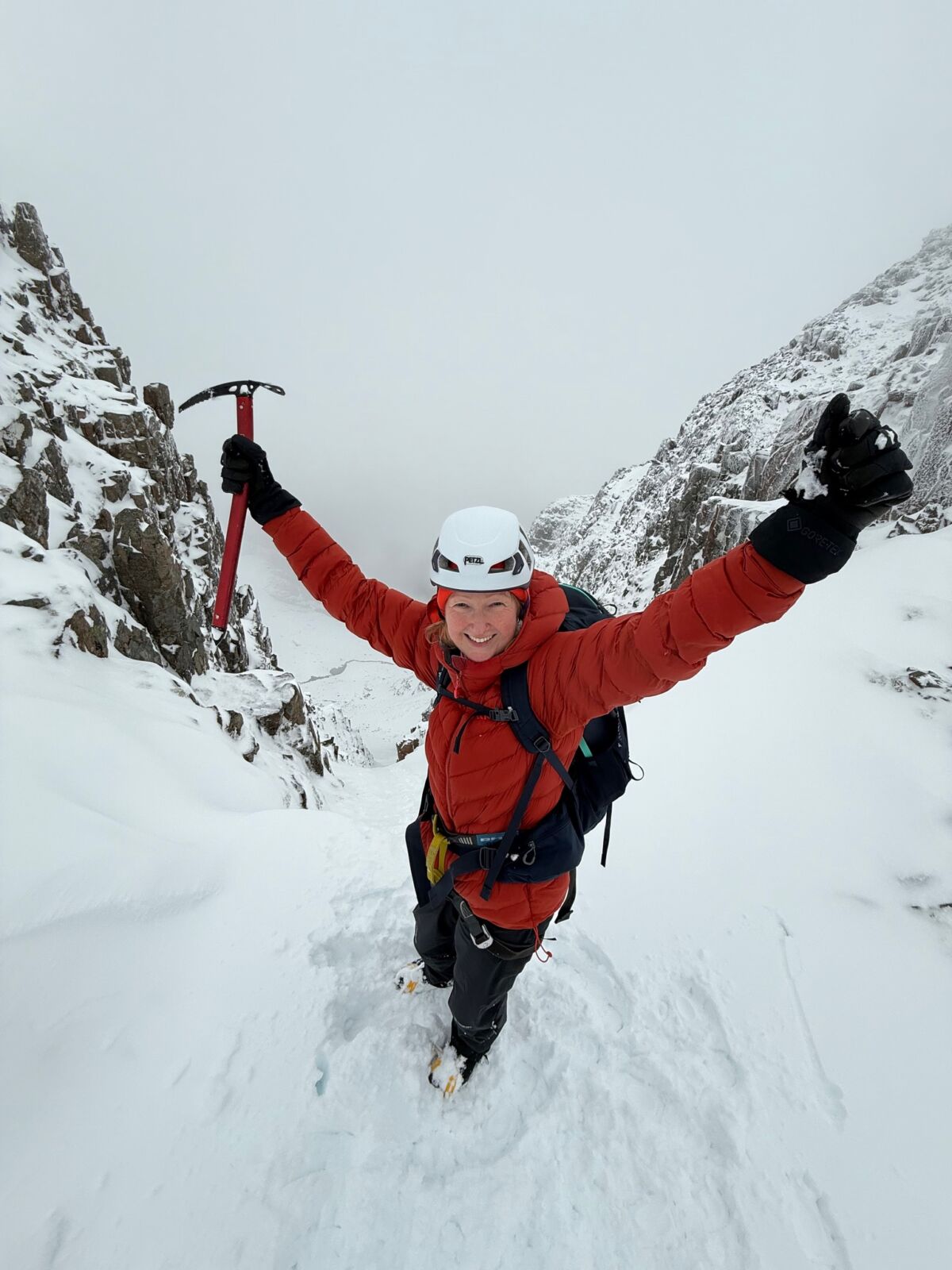 A lady with ice axe and crampons stands at the top of a steep gully on a guided winter walking course on Glencoe.