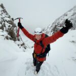 A lady with ice axe and crampons stands at the top of a steep gully on a guided winter walking course on Glencoe.