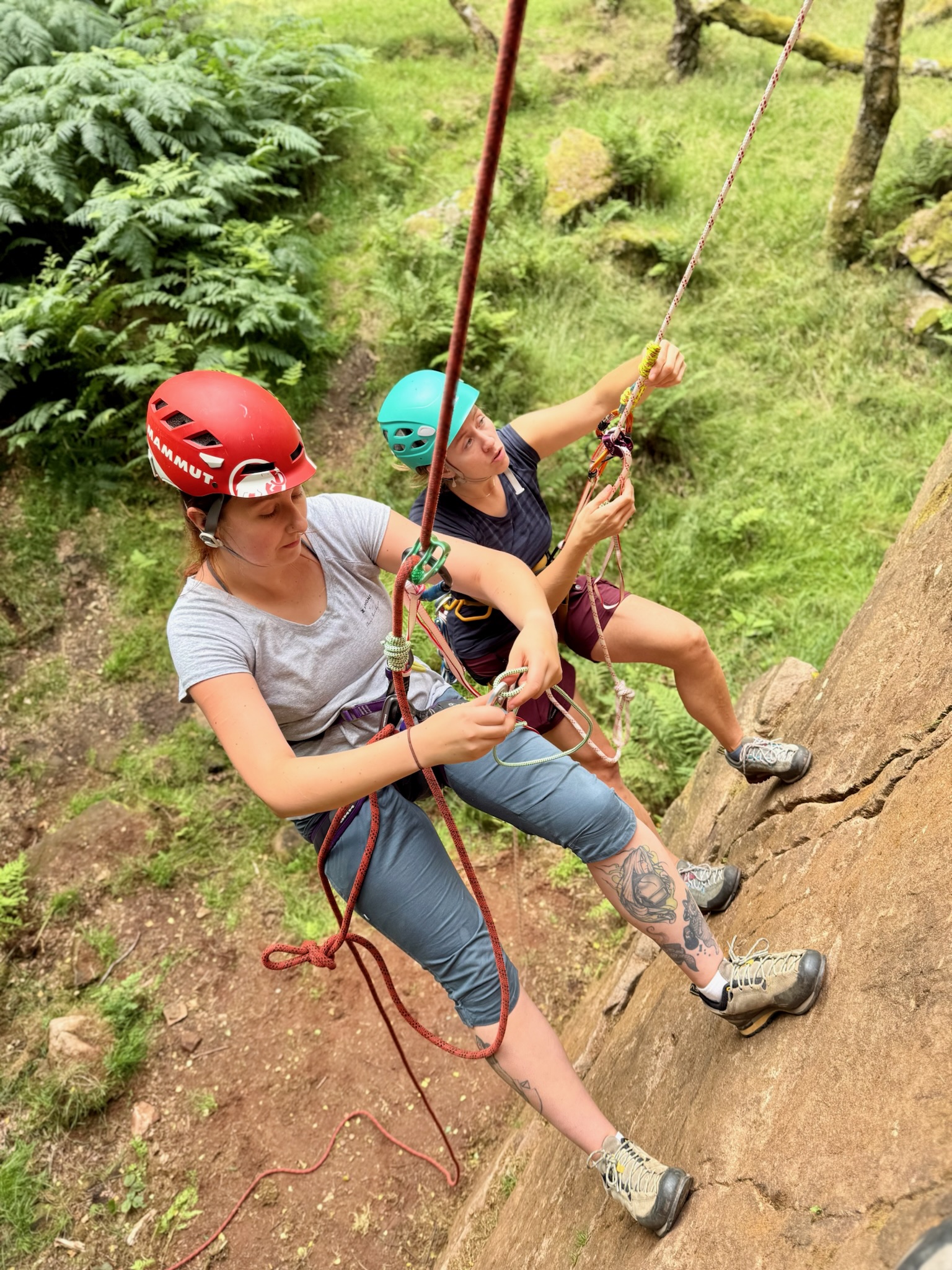 Two women climbers on a climbers self rescue course half way up a cliff in the Peak District.