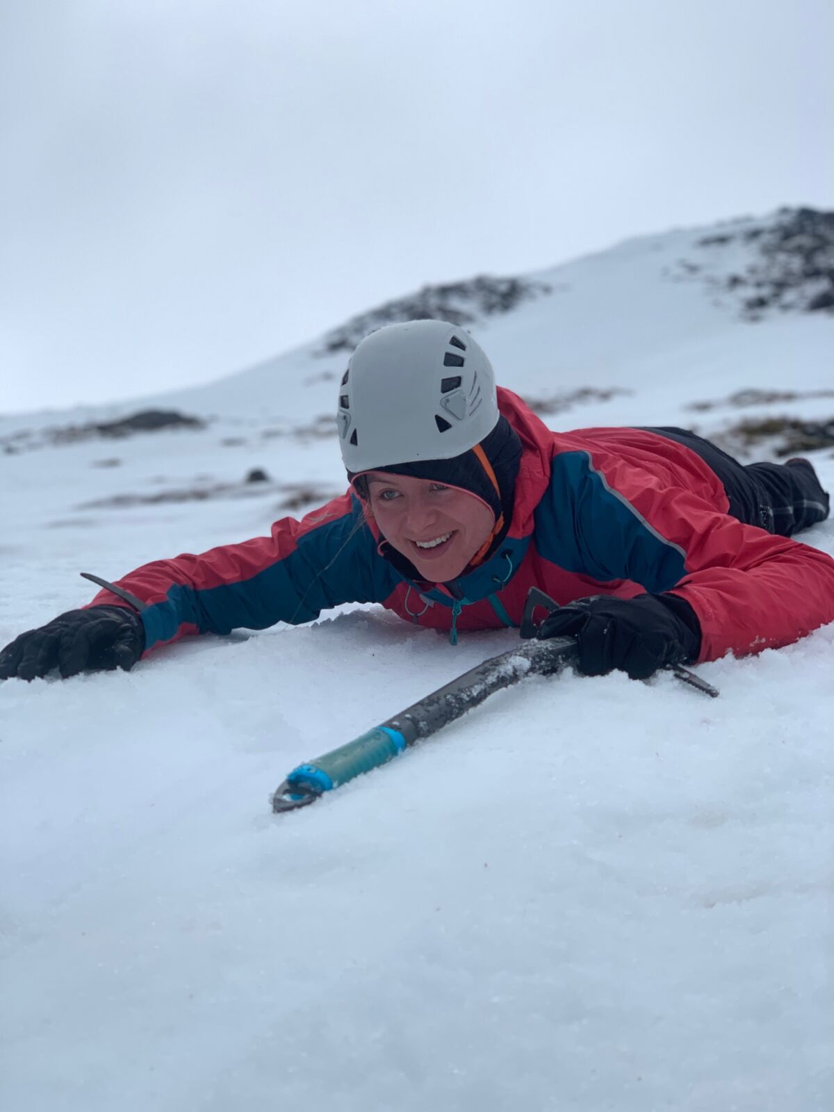 A lady lying face down on the snow learning to ice axe arrest on a Winter Skills course in Scotland.