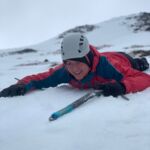 A lady lying face down on the snow learning to ice axe arrest on a Winter Skills course in Scotland.