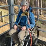 A man in a wheelchair about to abseil off a tower.