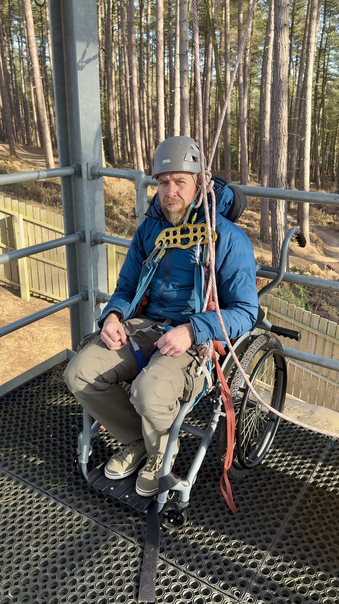 A man in a wheelchair about to abseil off a tower.