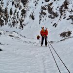 A lady abseils down a snow gully in Scotland on a winter climbing course.
