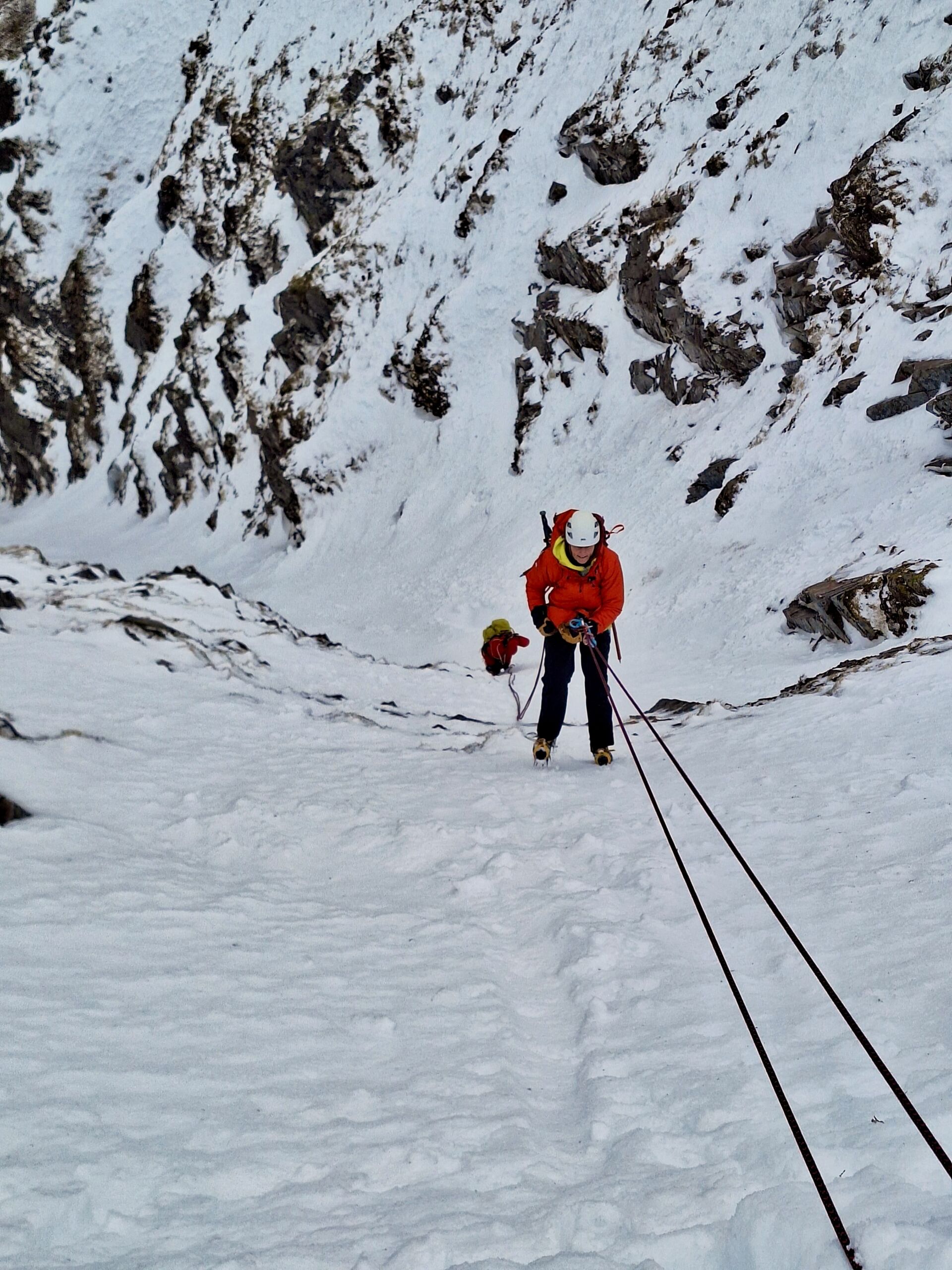 A lady abseils down a snow gully in Scotland on a winter climbing course.