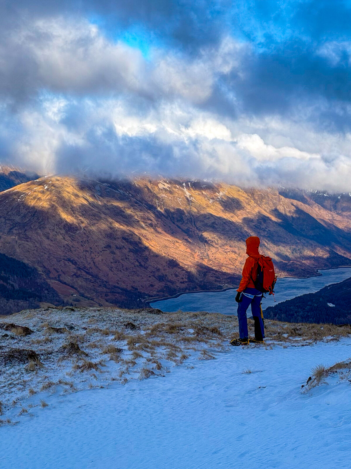 James looking out over Loch Leven in a red jacket clouds, mountains and loch in the distance
