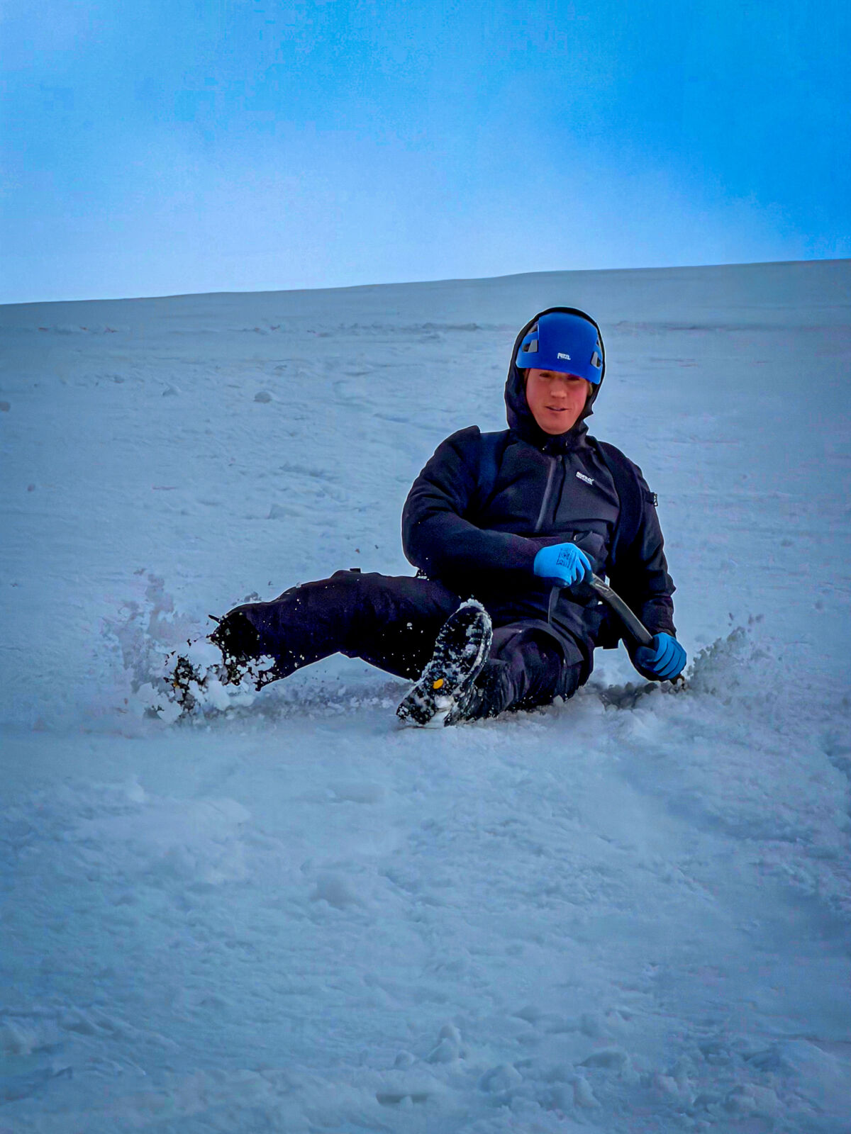 A man using an ice axe to self arrest on a winter skills course in Aviemore, Scotland.