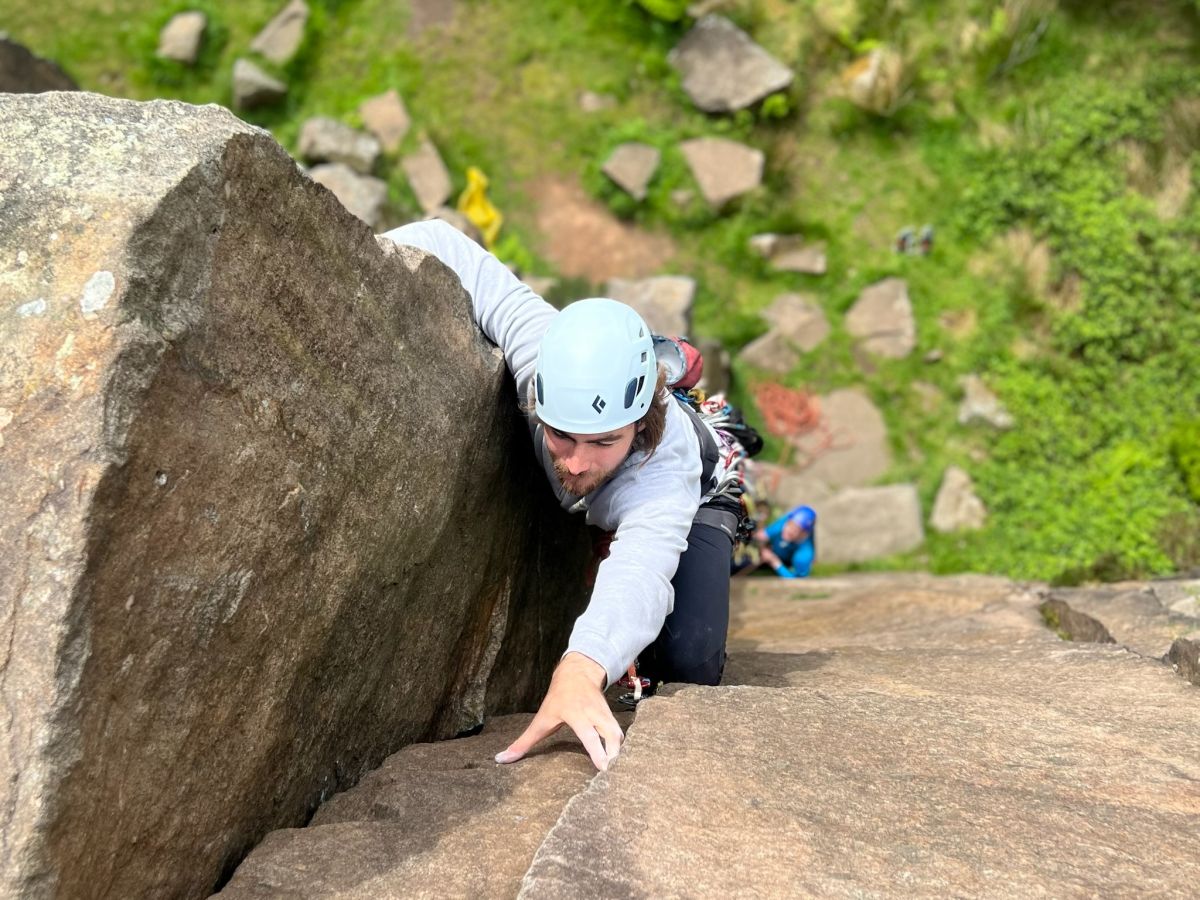 A man reaches the top of a rock climb, whilst learning to lead climb on a Beyond the Edge course in the Peak District.