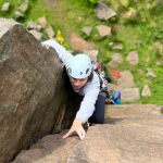 A man reaches the top of a rock climb, whilst learning to lead climb on a Beyond the Edge course in the Peak District.