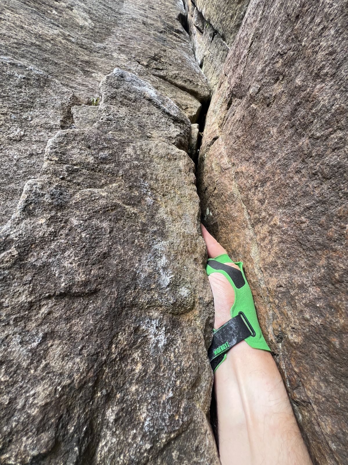 A hand wearing crack gloves is jammed in to a crack on a rock climb in the Peak District