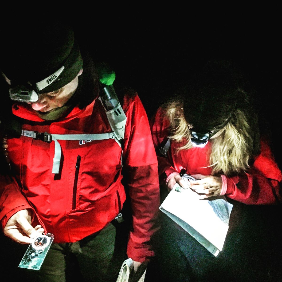 Two people in red jackets navigating and map reading at night wearing a head torch
